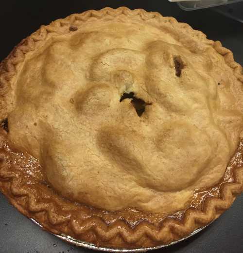 A freshly baked pie with a golden-brown crust and a decorative edge, resting on a dark surface.