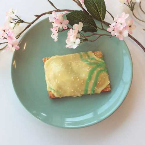 A frosted pastry on a teal plate, surrounded by delicate pink flowers.