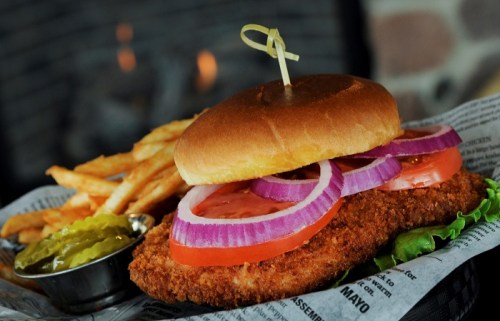 A crispy chicken sandwich with lettuce, tomato, and onion, served with fries and a side of pickles.