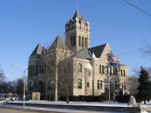 Historic stone courthouse with a clock tower, surrounded by trees and snow, under a clear blue sky.