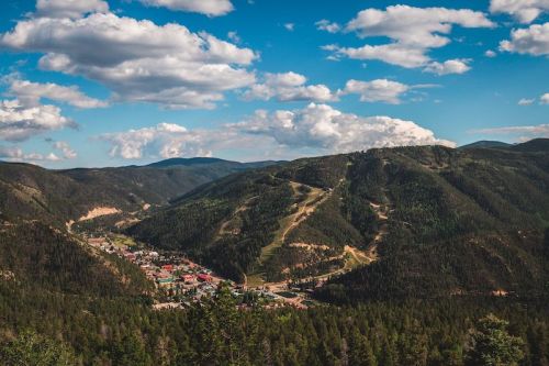 A scenic view of a mountainous landscape with a small town nestled in the valley, under a blue sky with fluffy clouds.