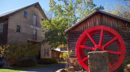 A historic old mill with a large red water wheel, surrounded by trees and blue sky.