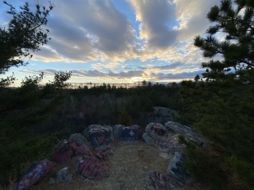 A scenic view of a sunset over a rocky landscape, framed by trees and clouds in the sky.