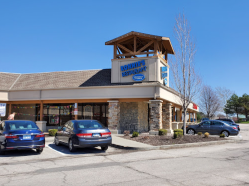 Exterior of Lottie's Restaurant featuring a stone facade and a wooden tower, with parked cars in front. Clear blue sky.