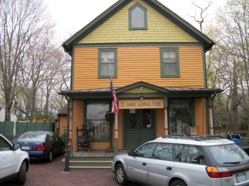 A colorful two-story building with a sign reading "St. James General Store," surrounded by trees and parked cars.