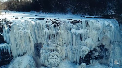 A frozen waterfall surrounded by snow-covered trees, showcasing icicles and a winter landscape.