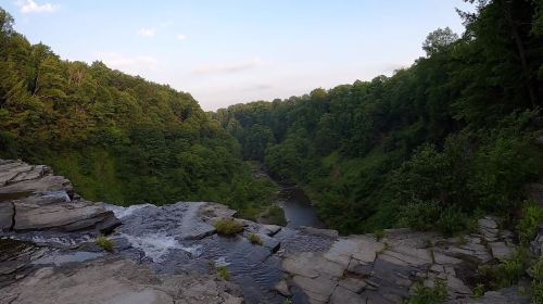 A scenic view of a waterfall cascading into a lush green valley surrounded by trees under a clear sky.