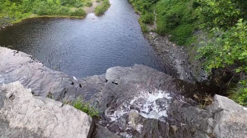A scenic view of a waterfall cascading into a calm river, surrounded by lush greenery and rocky terrain.