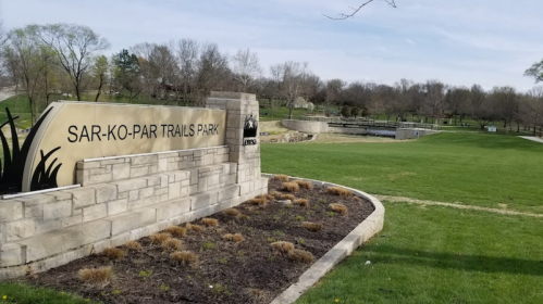 Sign for Sar-Ko-Par Trails Park with a grassy area and trees in the background.