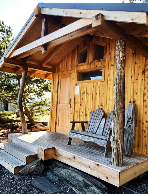A cozy wooden cabin with a porch and two chairs, surrounded by nature.