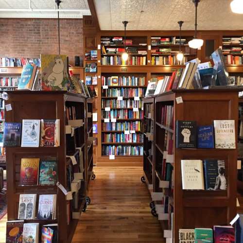 A cozy bookstore with wooden shelves filled with books, warm lighting, and a brick wall in the background.
