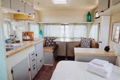 Cozy interior of a camper with a kitchenette, dining area, and a bed, featuring light colors and modern decor.