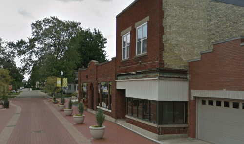 A brick building on a tree-lined street with planters and a garage, featuring a mix of architectural styles.