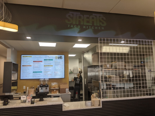 Interior of a taco kitchen with a menu board, staff preparing food, and a modern, clean design.