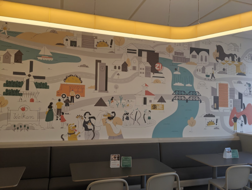 Colorful mural depicting a whimsical landscape with buildings, people, and nature, set in a cozy dining area.