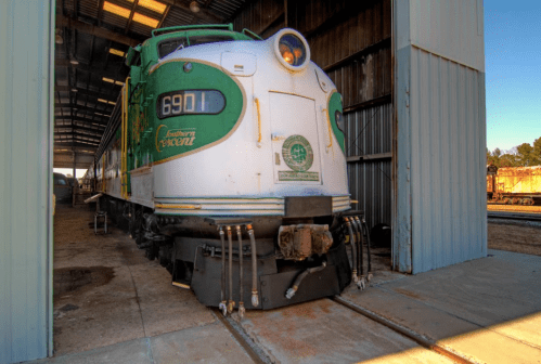 A vintage green and white locomotive parked inside a shed, partially visible with a concrete floor.