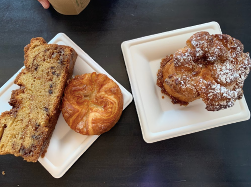 Two pastries on white plates: a slice of chocolate chip loaf and a flaky pastry dusted with powdered sugar.
