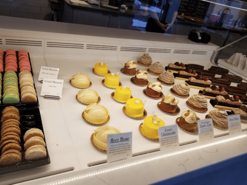 A display case filled with colorful macarons and various elegant pastries, including tarts and cheesecakes.