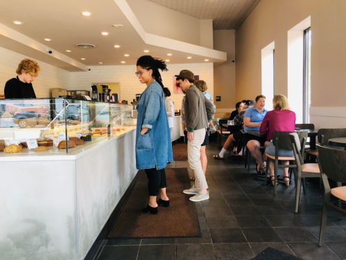 A cozy café scene with customers at the counter and others seated at tables, enjoying pastries and drinks.