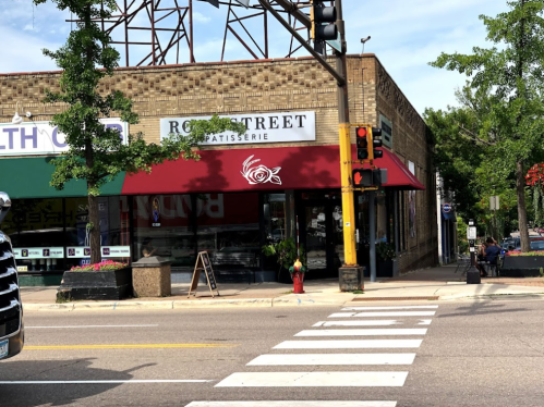 A street view of a patisserie with a red awning, next to a health store, and a traffic light in the foreground.