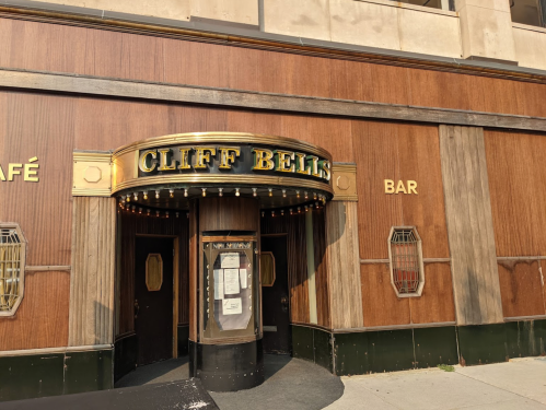 Entrance of Cliff Bell's, a vintage-style bar with wooden paneling and gold lettering, featuring a marquee and menu display.