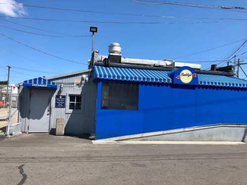 A blue building with a striped awning and a sign reading "Buddy's" on a sunny day, with power lines in the background.