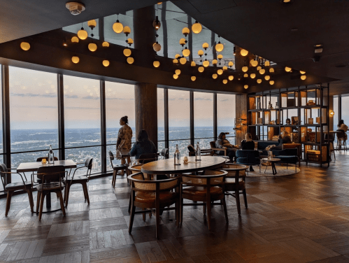 A modern restaurant with large windows, stylish furniture, and ambient lighting, offering a panoramic view.