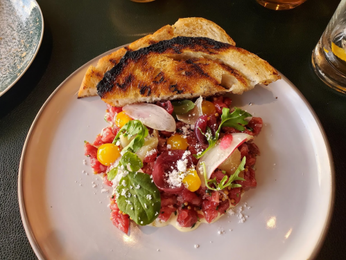 A plate of tartare topped with herbs and yellow tomatoes, served with charred bread on the side.