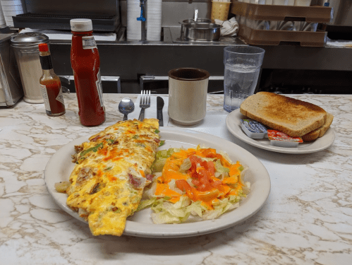 A plate with a vegetable omelet, salad, toast, and condiments on a marble table in a diner setting.