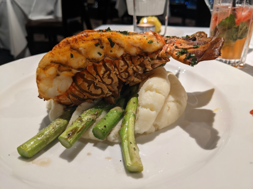 Grilled lobster tail atop creamy mashed potatoes and asparagus, served on a white plate.