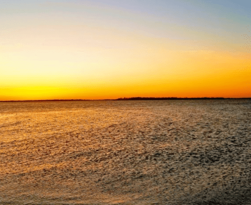 A serene sunset over a calm body of water, with warm orange and yellow hues reflecting on the surface.