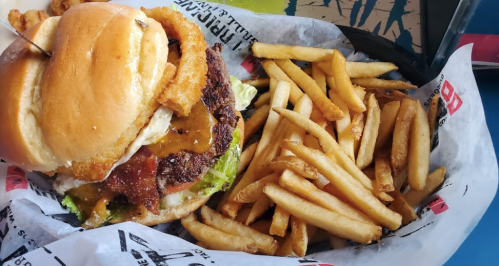 A juicy burger with lettuce, bacon, and onion rings, served with a side of crispy French fries on a tray.