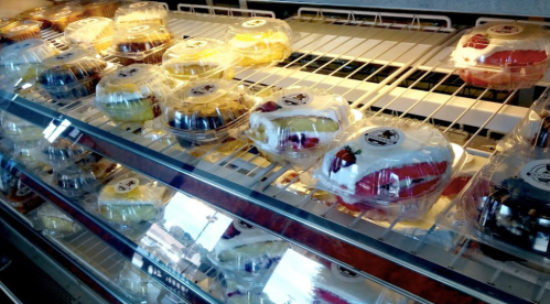A display case filled with colorful, individually packaged desserts topped with cream and fruit.