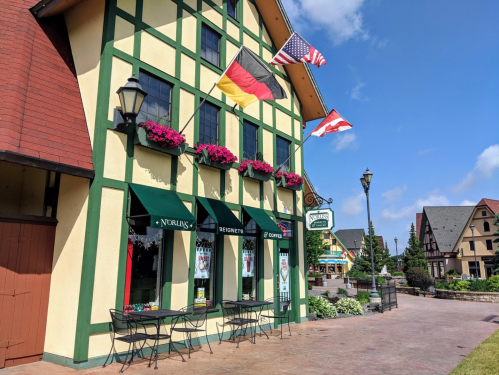 A charming building with German and American flags, flower boxes, and outdoor seating in a quaint village setting.