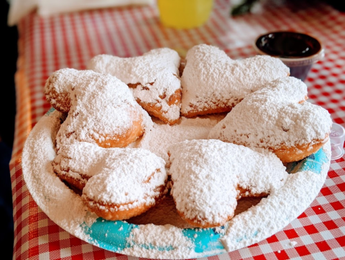 A plate of heart-shaped pastries dusted with powdered sugar, arranged on a checkered tablecloth.