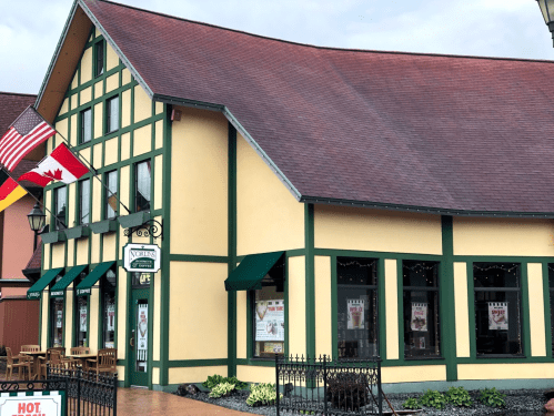 A colorful building with a steep roof, featuring flags and outdoor seating, set in a charming town square.