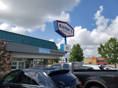 Sign for Randy's University Store with a blue sky and clouds in the background, surrounded by parked cars.