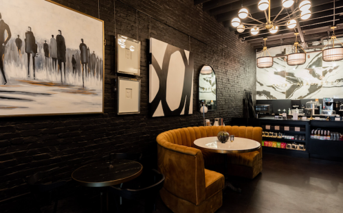 A stylish café interior featuring a curved orange sofa, modern art, and a coffee counter against a dark brick wall.