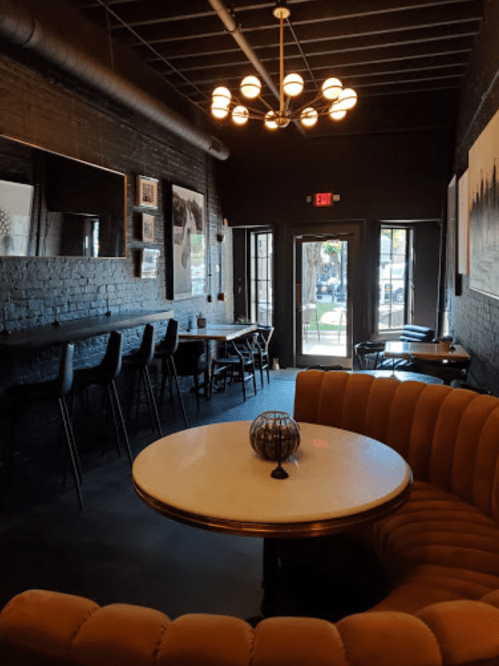 Cozy café interior with a round table, curved seating, and modern lighting, featuring large windows and a welcoming atmosphere.