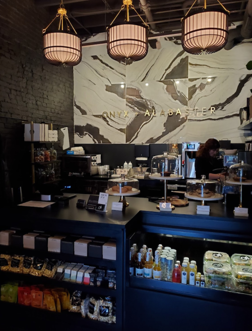 A stylish café interior with a dark counter, pastries on display, and pendant lights hanging from the ceiling.