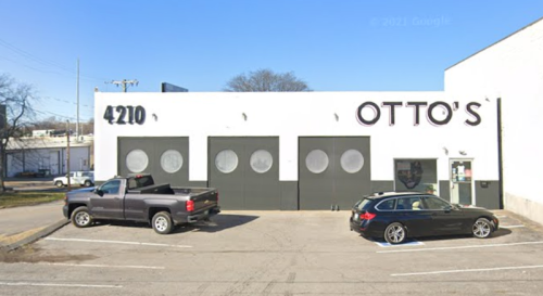A building with the name "OTTO'S" on the front, featuring three garage doors and two parked vehicles in the lot.