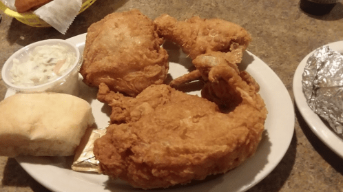 A plate of fried chicken with two pieces of chicken, a biscuit, coleslaw, and a foil-wrapped item on the side.