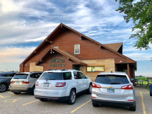 A wooden building labeled "House of Coates" with several parked cars in front under a cloudy sky.