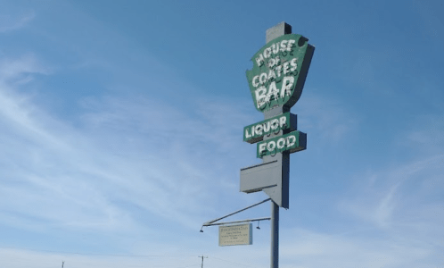 Sign for Coates Bar featuring "Liquor" and "Food" under a clear blue sky.