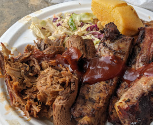 A plate of barbecue featuring pulled pork, ribs with sauce, coleslaw, and a piece of cornbread.