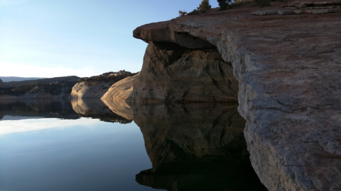 A serene landscape featuring a rocky cliff reflecting in calm water under a clear sky.