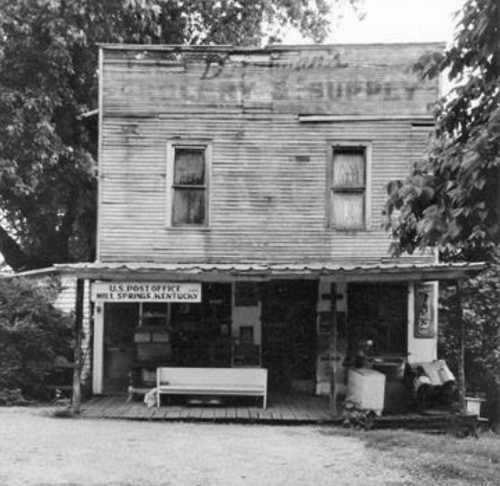 Black and white image of a vintage general store with a porch, featuring a sign for the U.S. Post Office in Mill Springs, Kentucky.