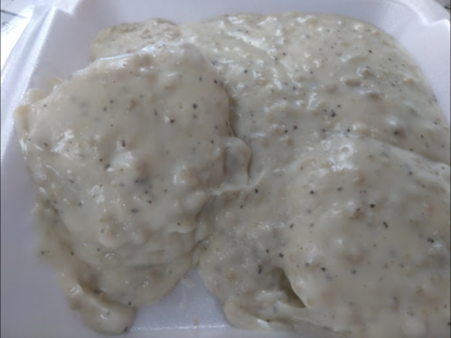 A close-up of creamy, peppered gravy served over two pieces of soft, fluffy biscuits in a takeout container.