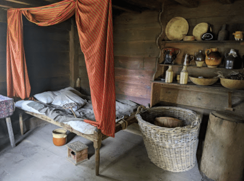 A rustic bedroom with a wooden bed, colorful drapes, and shelves filled with pottery and woven baskets.