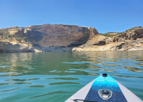 A kayak on calm water with rocky cliffs and blue sky in the background.